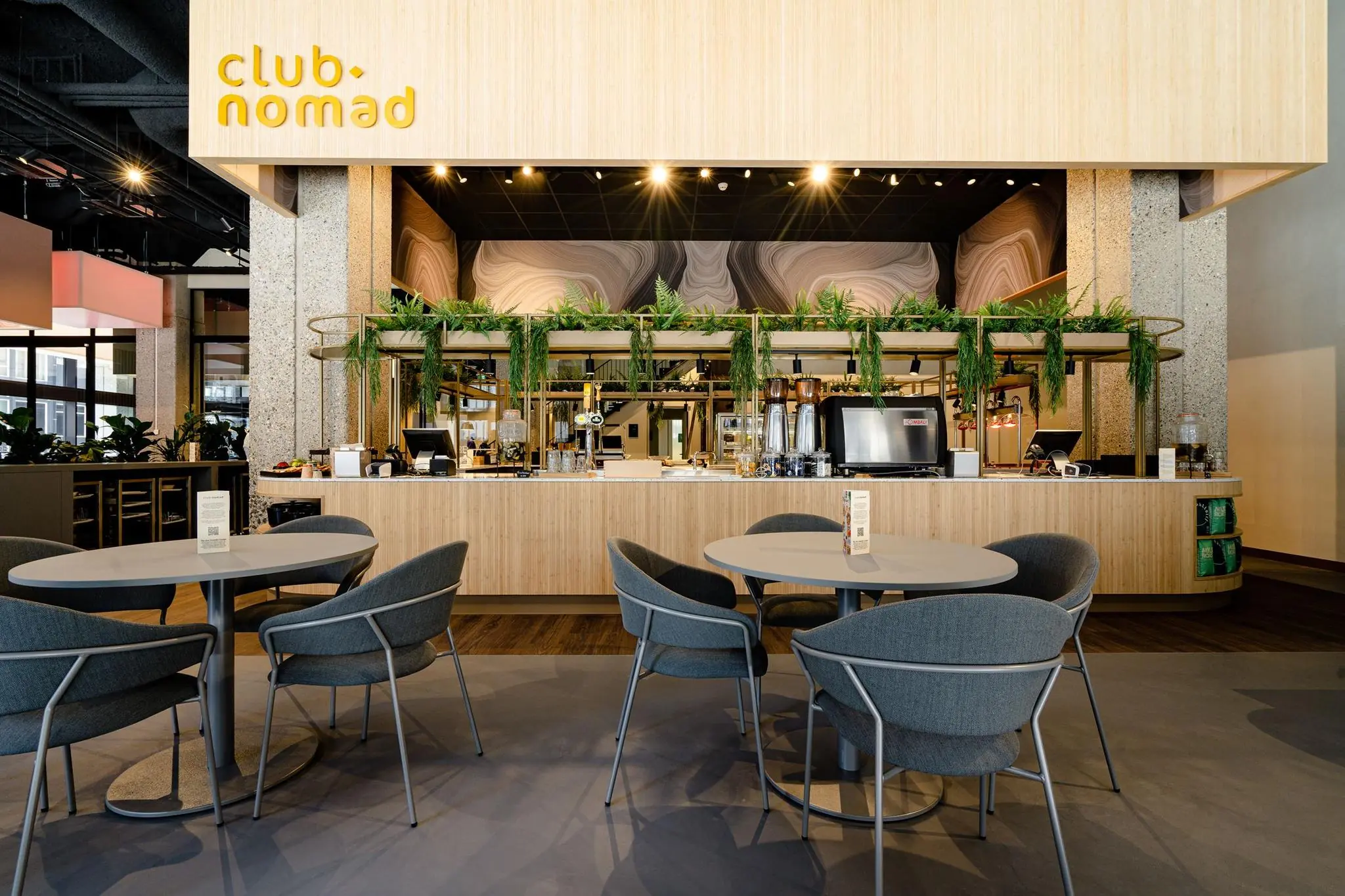 Moderne horecaruimte van Club Nomad aan de Aert van Nesstraat met stijlvolle zitplaatsen en een bar met groene accenten.